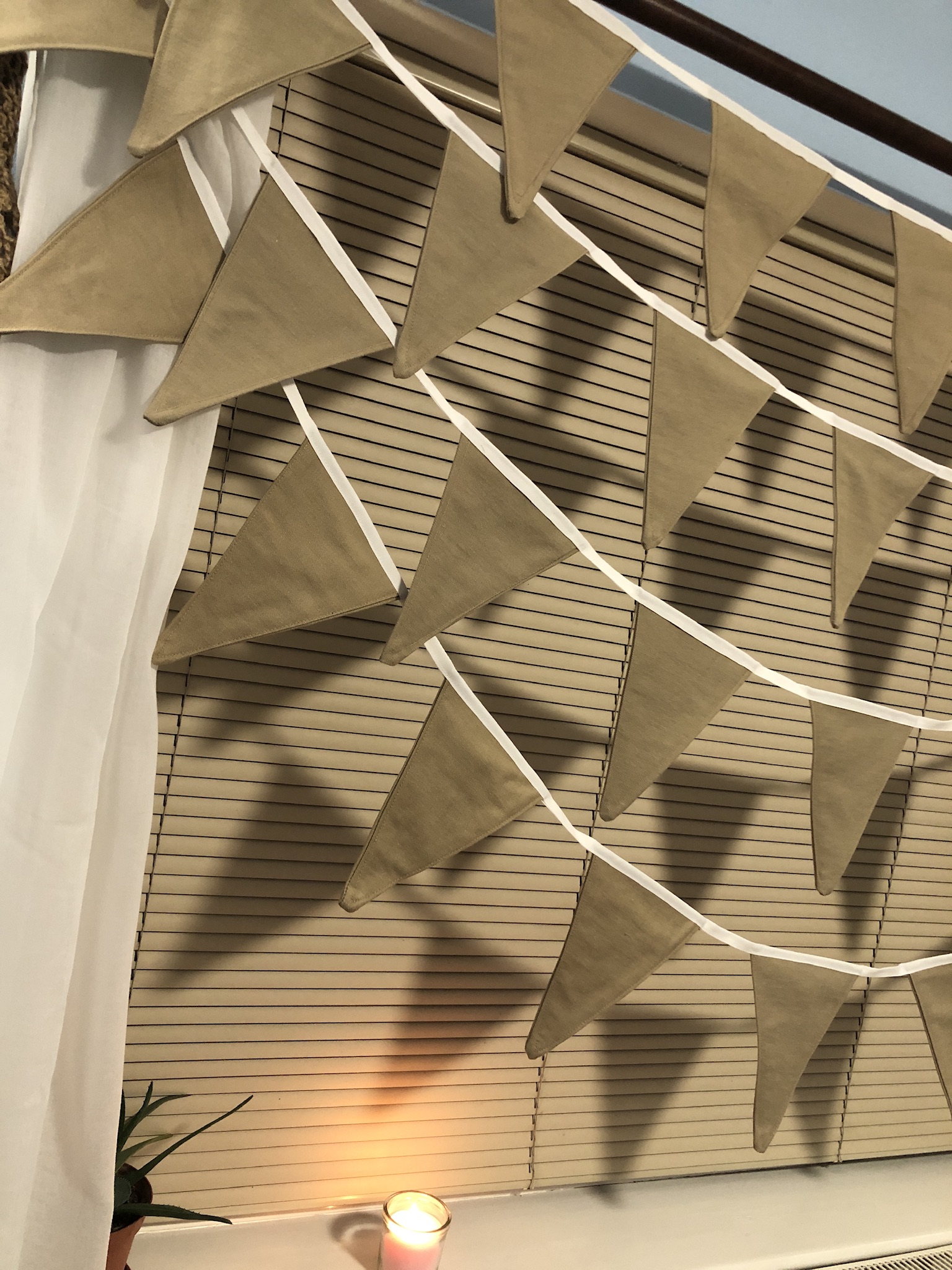 100% cotton bunting in beige, similar to the colour of hessian. Lovely natural tones. 4 rows of beige bunting hanging at a window. Natural tones, hessian type colour.