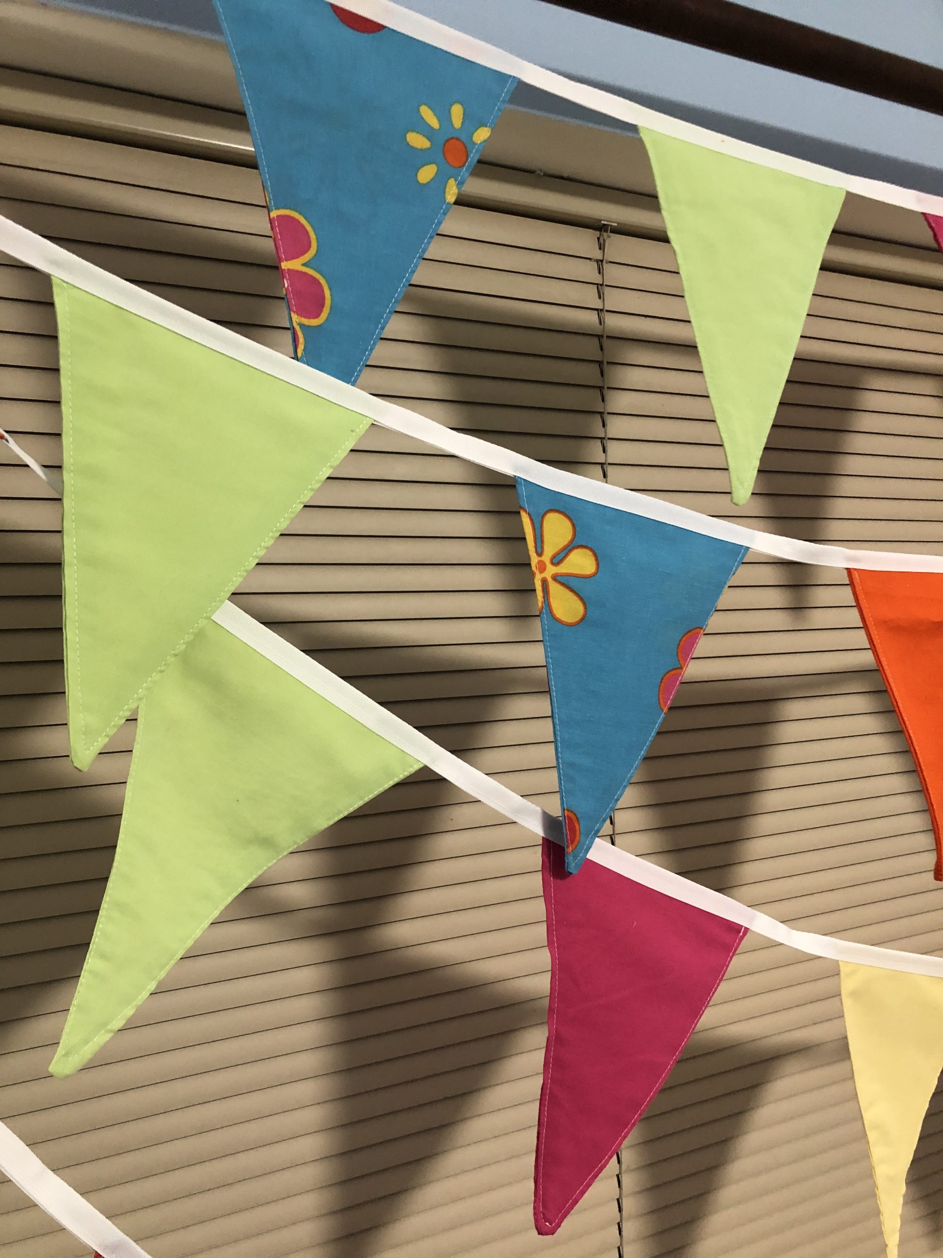 10 meters of brightly coloured bunting. Flags are orange, lime green, bright pink and a 60s style flowered pattern on mid blue.